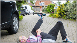 A girl laying down with her foot in the air with a girl in the background looking to be balancing on the other girls foot.