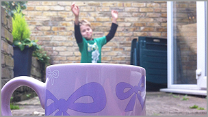 A boy in a green t-shirt using a perspective technique to make it look like he's floating in a mug