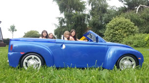 A group of kids behind a toy car so they look like they are driving it