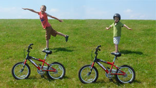 2 kids standing behind their bikes so it looks like they are standing on the saddle