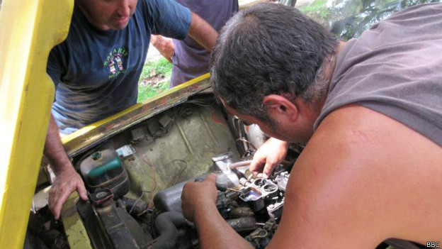 Un grupo de hombres tratan de reparar el carburador de un Lada.